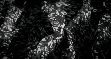 Soyut desenleri ve yumuşak kıvrımları olan gri tonlu bir kumaşın bulanık görüntüsü dinamik ve sanatsal bir görsel etki yaratıyor. Işık ve karanlık tonlar arasındaki zıtlık derinlik ve boyut ekler..