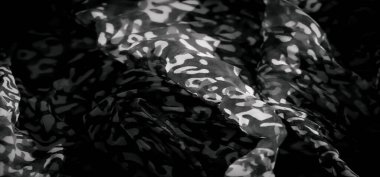 Soyut desenleri ve yumuşak kıvrımları olan gri tonlu bir kumaşın bulanık görüntüsü dinamik ve sanatsal bir görsel etki yaratıyor. Işık ve karanlık tonlar arasındaki zıtlık derinlik ve boyut ekler..