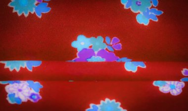 Pürüzsüz kırmızı kumaş, parlak mavi ve mor çiçek aksanıyla kaplanmış. Canlı çiçek tasarımı kumaşın yumuşak kıvrımlarıyla güzel bir tezat oluşturuyor ve desene sanatsal bir dokunuş ekliyor.