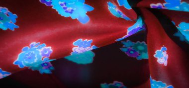 Mavi ve mor çiçek desenleriyle süslenmiş canlı kırmızı kumaş bulanıklığı. Yumuşak kıvrımlar ve parlayan çiçekler karmaşık tasarım detaylarını vurgulayan büyüleyici bir kontrastlık yaratır..