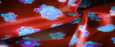 Çarpıcı mavi ve mor çiçek desenleri gösteren lüks kırmızı bir kumaşın bulanıklığı. Canlı çiçekler zengin arka planda göze çarpıyor, kumaşın dokusuna derinlik ve zarafet katıyor..