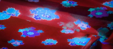 Pürüzsüz kırmızı kumaş. Parlayan mavi ve mor çiçeklerle vurgulanmış. Parlayan çiçek motifleri kumaş yüzeyinde süzülüyor, görsel olarak çarpıcı ve zarif bir tasarım yaratıyor..