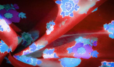 Parlayan çiçek izleriyle kaplı kırmızı kumaş lekeleri. Mavi ve mor çiçekler görsel cazibeyi arttırır, pürüzsüz kumaşı tamamlayan parlak bir etki yaratır..