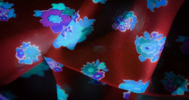 Pürüzsüz kırmızı kumaşta parlayan parlak mavi ve mor çiçek motifleri. Kumaşın kıvrımları derinlik ve doku yaratır, yumuşak maddeye karşı parlak çiçekli tasarımı vurgular..