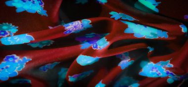 Parlayan mavi ve mor çiçek desenleri parlak kırmızı kumaşa yayılmış. Kumaşın yumuşak kıvrımları ve dokusu, genel estetiğe zarafet katarak parlak çiçek tasarımını vurgular..