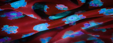 Parlayan mavi ve mor çiçek desenleri parlak kırmızı kumaşa yayılmış. Kumaşın yumuşak kıvrımları ve dokusu, genel estetiğe zarafet katarak parlak çiçek tasarımını vurgular..