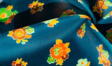 Koyu turkuaz bir arka planda parlak turuncu, yeşil ve sarı çiçekli koyu renkli bir çiçek kumaşı. Materyalin kıvrımları bir hareket ve akış hissi yaratır ve tasarımı mükemmelleştirir.