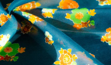 Bulanık görüntü, parlak yeşil, turuncu ve sarı desenleri zengin mavi kumaşa karşı sergiliyor. Doku yumuşak ve narin, üst üste gelen kıvrımlar derinlik ve hareket hissi yaratıyor.