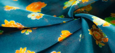 Hassas turuncu, sarı ve yeşil çiçek desenli mavi kumaş. Zengin mavi arka plandaki canlı çiçekler çarpıcı ama uyumlu bir karşıtlık yaratır..