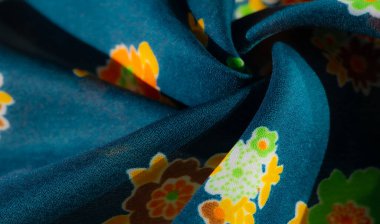 Turuncu, yeşil ve sarı renkli canlı çiçek desenleri zengin bir turkuaz kumaşa yayılarak hoş ve canlı bir kontrast oluşturuyor. Kumaştaki kıvrımlar derinlik ve doku ekler..