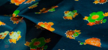 Koyu mavi arka planda sarı, turuncu ve yeşil çiçek desenli canlı bir kumaş. Kumaşın yüzeyinin yumuşak bir dokusu vardır ve renkli çiçekler çarpıcı bir kontrast yaratır..