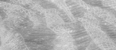 Beyaz kumaş üzerine ince dantel işçiliği, karmaşık ve hassas desenler sergiliyor. Hafif dokusu, hafif bir parıltıyla, kumaşın zarafetini ve inceliğini arttırır.