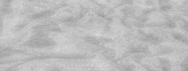 İnce dokunmuş beyaz dantel kumaş bulanıklığı. Malzemenin havadar ve şeffaf niteliklerini gösteriyor. Dantel, yumuşaklık ve zarafet hissi veren karmaşık desenler oluşturur..