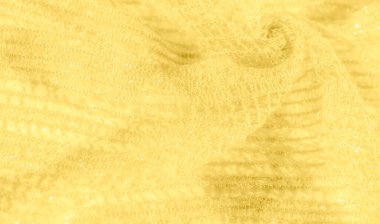 Işıldayan, ışıldayan bir dokusu olan sarı kumaş bulanıklığı. Karmaşık dokuma ve yumuşak kıvrımlar ışığı yansıtıyor, yüzey boyunca parlak, altın bir etki yaratıyor..