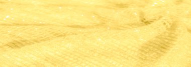 Işıldayan, ışıldayan bir dokusu olan sarı kumaş bulanıklığı. Karmaşık dokuma ve yumuşak kıvrımlar ışığı yansıtıyor, yüzey boyunca parlak, altın bir etki yaratıyor..