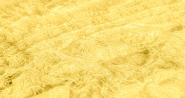 Işıl ışıl parlak ipliklerle parıldayan sarı bir kumaşın bulanıklığı. Narin doku ışığı yakalar, zarif kıvrımları ve yumuşak yüzeyi arttıran parlak ve yansıtıcı bir desen yaratır..