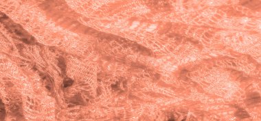 Karmaşık dokuma deseni ve ışıltılı dokusu olan şeftali rengi dantel kumaştan bulanık bir kare. Yumuşak ışıklandırma, ince işçiliği ve kumaşın şeffaf kalitesini ön plana çıkarıyor..