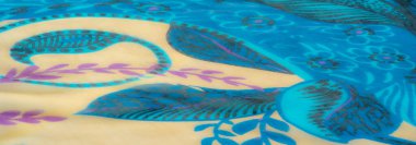 Yumuşak bej, mor ve deniz mavisi desenli karmaşık çiçek desenli, lüks mavi kumaş. Krem püskülleri ile aksanlı, dinamik ve desenli bir tekstil kompozisyonu yakalıyor.