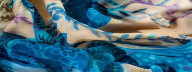 Mavi ve bej tonlarında çiçekli ve soyut tasarımlı zarif bir kumaşın bulanıklığı. Sınır boyunca uzanan ponpon detayları akan tekstile eğlenceli bir dokunuş ekler.