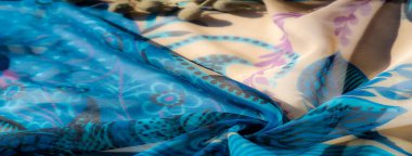 Görüntü. Yumuşak, akışkan mavi kumaş bej kısımlarla birleştirilmiş, karmaşık mor ve mavi desenler sergiliyor. Kumaşlar nazikçe katlanır ve hassas dizayn görsel olarak tatmin edici olur.