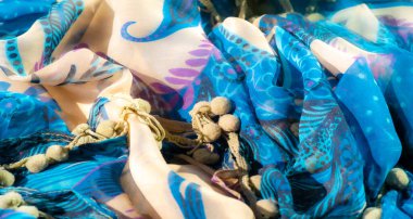 Canlı mavi kumaşın bulanık, narin mor çiçek aksanları ve akıcı bej kıvrımları var. Karmaşık tasarım ve doku görsel olarak dinamik bir tekstil yaratır..