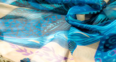 Bej aksanlı mavi kumaş bulanıklığı. Karmaşık çiçek desenleri ve püskülleri var. Pürüzsüz ve akıcı dokusu dekoratif detaylarla birleşince sanatsal ve şık bir tasarım yaratıyor..