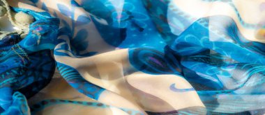 Bej aksanlı mavi kumaş bulanıklığı. Karmaşık çiçek desenleri ve püskülleri var. Pürüzsüz ve akıcı dokusu dekoratif detaylarla birleşince sanatsal ve şık bir tasarım yaratıyor..