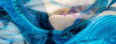 Bej aksanlı narin mavi kumaşın bulanıklığı, girdap şeklinde soyut bir çiçek deseni sergiliyor. Yumuşak madde büyüleyici bir akış yaratır, mor ve siyah detaylar kontrastı ekler..