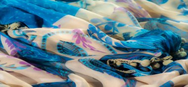 Bej aksanlı narin mavi kumaşın bulanıklığı, girdap şeklinde soyut bir çiçek deseni sergiliyor. Yumuşak madde büyüleyici bir akış yaratır, mor ve siyah detaylar kontrastı ekler..