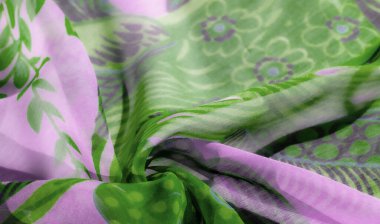 Parlak yeşil ve yumuşak lavanta tonlarında girdap desenleri olan hassas bir kumaşı gösteren bulanık bir görüntü. Sıvı tasarımı, kumaşa hava hissi veren yaprak motifli botanik baskılar içeriyor..
