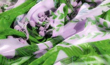 Soyut botanik desenleri olan yeşil ve lavantalı bir tekstil, akış dokusunu vurgulamak için yumuşakça örtülmüş. Moda veya iç tasarım projelerine sanatsal bir dokunuş eklemek için ideal.