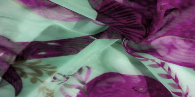 Nane yeşili kumaşa zıt mor çiçek desenleri. Yumuşak ve akıcı bir dokuyu karmaşık soyut tasarımlarla göstererek canlı ve narin bir görünüm yaratıyor..