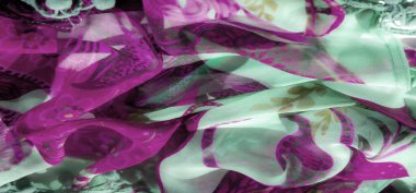 Yumuşak bir nane yeşili kumaş üzerinde dönen mor çiçeklerin ve yapraklı aksanların bulanıklığı. Hassas tasarım, tekstil için çağdaş ama kadınsı bir dokunuş sunan soyut biçimlerle kaplıdır..