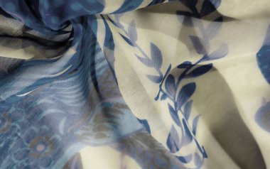 Mavi ve bej bir kumaşın bulanıklığı çiçek desenleri ve soyut girdap desenleri. Akan, şeffaf kumaş herhangi bir tekstil veya moda projesine yumuşaklık ve zarafet getirir..