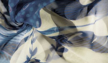 Yumuşak bej aksanlar ve soyut girdaplarla sarmalanmış narin yaprak desenleri olan mavi çiçekli bir kumaşın bulanıklığı. Kumaşın dokusu, mavi ile harmanlanmış durgun ve akışkan bir hareket sağlar.