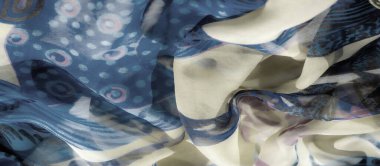 Mavi ve bej kumaş üzerinde soyut desenlerin bulanıklığı yumuşak ve zarif bir renk etkileşimi yaratıyor. Kumaşlar nazikçe katlanır ve ince tasarımlar sakin, akıcı bir estetik yayar.