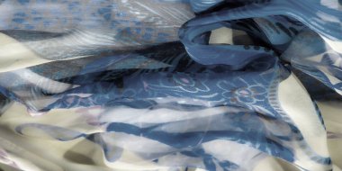 Çiçekli ve soyut desenli canlı mavi ve bej kumaş bulanıklığı. Akan kumaş renklerin hassas ve sanatsal etkileşimini ortaya çıkararak hareket hissi yaratıyor..