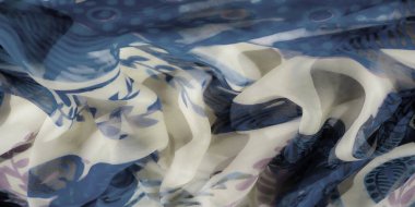 Soyut mavi ve krem kumaşlı, çiçek desenli, geometrik desenli bir bulanıklık. Yumuşak doku ve akışkan kıvrımlar sanatsal ve dinamik bir kompozisyon oluşturur..