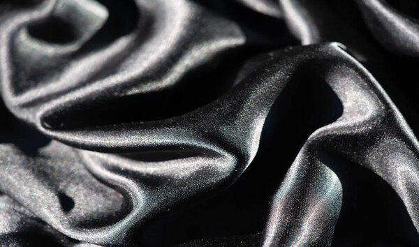 Размытие скрученной черной ткани, образующей сложные волны и складки. Блестящая поверхность улавливает свет, создавая игру между блеском и глубокими тенями в этой элегантной абстрактной композиции.