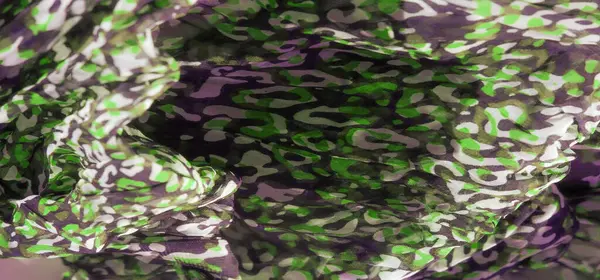 Saf kumaş üzerinde yeşil, siyah ve beyaz desenli soyut bir kamuflaj tasarımı. Dinamik akış ve kalın renkler göz alıcı bir görsel cazibe yaratır..