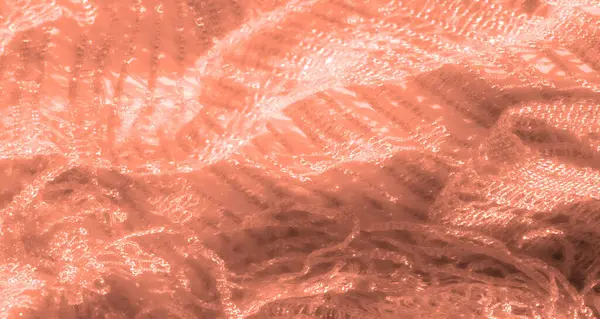 Şeftali dantelli kumaş, ince detaylar ve parlak aksanlı bulanık bir yakın plan. Karmaşık dokuma deseni ve ince ışık oyunu kumaşın tasarımına zarafet ve doku ekler..