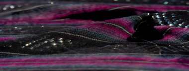 Çizgili kumaş tasarımı bulanık koyu siyah, pembe ve mavi renkte kumaşlar ve karmaşık iplikler içeriyor. Zengin renk zıtlıkları ve parıldayan detaylar derinlik yaratır