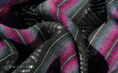 Koyu pembe ve turkuaz çizgili desenli siyah kumaş. Buruşuk yüzey derinlik ve görsel ilgi ekliyor. İnce parıltılı detaylar materyale yayılıyor..