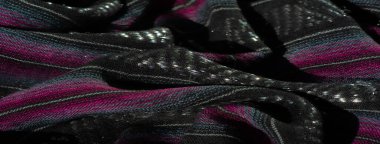 Karmaşık bir siyah kumaş bulanıklığı. Dokuda canlı pembe ve turkuaz çizgiler var. Kumaş dinamik kıvrımlar halinde kıvrılır ve parlak detaylarına ışık tutar..