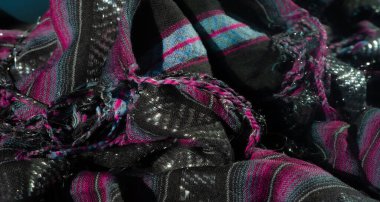 Pembe ve mavi çizgili katlanmış siyah kumaşların bulanık yakın çekimi karmaşık dokular ve ince yansıtıcı desenler içeriyor. Kumaş, zıt renklerle zengin bir görsel cazibe yaratıyor.