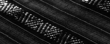 Çapraz dokuma desenleri ve yansıtıcı yüzeyleri olan bulanık siyah beyaz kumaş. Kumaş dokusu ışık oyunuyla derinlik yaratırken, geometrik tasarımlar karmaşıklık ve ilgi ekliyor..