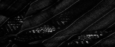 Karmaşık çizgili ve geometrik desenli siyah bir kumaşın bulanık yakın çekim görüntüsü. Kumaş yüzeyinde hafif gölgeler ve gölgeler yaratan bir ışık oyunu sergiler..