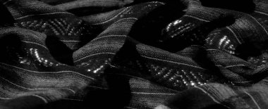 Çapraz dokuma desenleri olan parlak siyah kumaşın bulanık yakın çekimi. Kumaşın dokusu ve parlaklığı stratejik ışıklandırmayla vurgulanır. Pürüzsüz ve lüks bir görünüm yaratır..