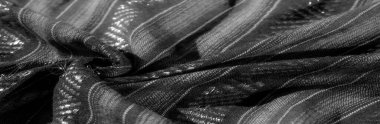 Karmaşık dokuma desenleri ve parlak yansıtıcı detayların birleşiminden oluşan siyah bir kumaşın bulanık görüntüsü. Doku derinlik ve boyut ekler. Işıklar kumaşın zarafetini arttırır..