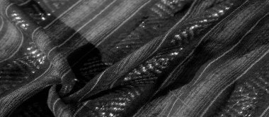 Çapraz geometrik deseni ve ince parlaklığı olan desenli siyah ve gri bir kumaşın bulanık görüntüsü. Karmaşık tasarımda ışığın etkileşimi derinlik yaratır ve dokuma dokusunu vurgular..